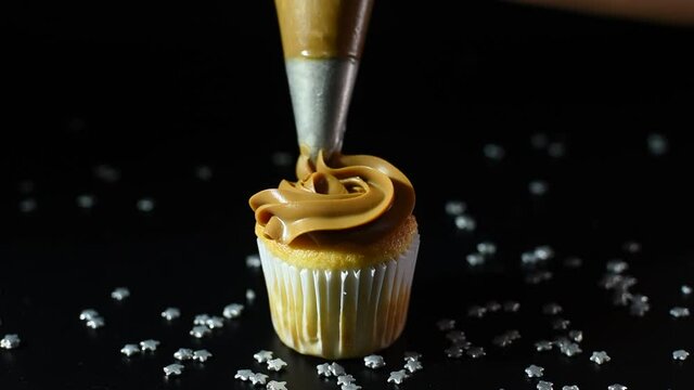
pastry decorating a cupcakes with dulce de leche with a pastry bag on a black background
