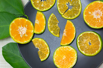 The tangerine sliced is placed in a black dish and the edge of the dish has green orange leaves.