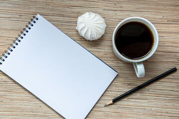 A cup of coffee with marshmallow, notebook with pencil on wooden background. Cosy workspace. Top view, flat lay