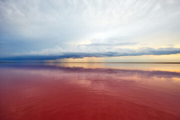 pink lake and sandy beach with a sea bay under a blue sky with clouds