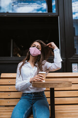 Woman in a medical mask drinks coffee on the street