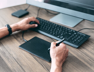 A man creates a design on a graphic tablet. He holds a stylus in his hand. Rear view