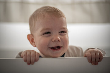 Bebé varón en su cuna riendo y mirando hacia su izquierda