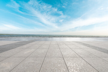 Empty square floor and lake under blue sky.