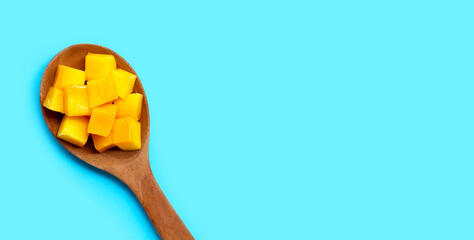 Sliced ripe mango cubes on wooden spoon on blue background.
