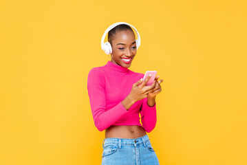 Fashionable happy African American woman wearing headphones listening to music from smart phone on...