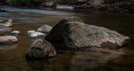 small river in forest with stones at sunset