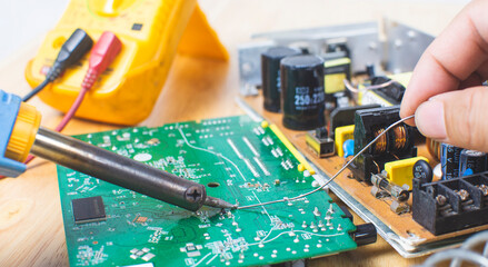 Technician is using electric soldering iron and the tin for repairing electronic circuit board