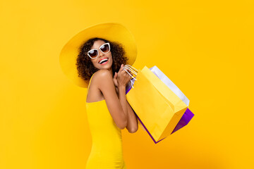Happy surprised woman with colorful shopping bags smiling on yellow background for summer sale...