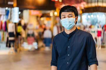 Fototapeta na wymiar young asian man wearing medical mask at shopping mall for prevention from coronavirus (Covid-19) pandemic. new normal concepts