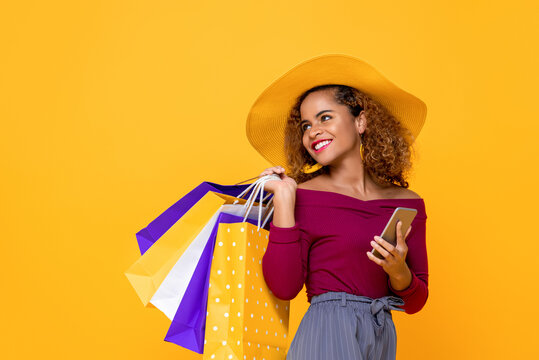 Fashionable Smiling Mixed Race Woman With Colorful Shopping Bags And Mobile Phone Isolated On Yellow Background For Summer Sale Conept