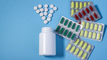 Bottle and scattered pills on color background, top view. Space for text. white plastic bottl ith scattered white and multi-colored pills and capsules on a blue background.Space