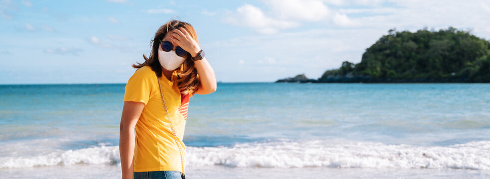 Young asian woman tourist wearing protective face mask travel on the beach in Thailand summer Corona virus travel corona virus spread prevention.background panoramic