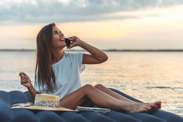 Young woman in straw hat talking to the smartphone on a beach.