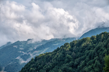 High mountain with green slopes hidden in clouds and fog. Green mountain slope with cable cars and ski runs at overcast summer day.