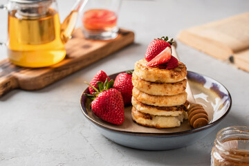 Cottage cheese pancakes with honey and fresh strawberries in a beautiful plate on a light background. Breakfast. Russian and Ukrainian cuisine.