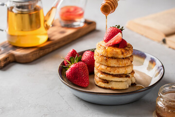 Cottage cheese pancakes with honey and fresh strawberries in a beautiful plate on a light background. Breakfast. Russian and Ukrainian cuisine.