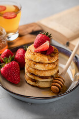 Cottage cheese pancakes with honey and fresh strawberries in a beautiful plate on a light background. Breakfast. Russian and Ukrainian cuisine. Copy space