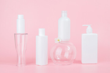Set of care cosmetic for skin, face, body or hair. White blank cosmetics bottles and tube on glass podiums, pink background. Spa Cosmetic Beauty Concept. Front view Mockup