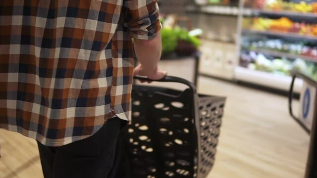 Rare view of man with a shopping trolley walks in a supermarket, entrance. Cropped footage of the trolley and consumer in focus, blurred background
