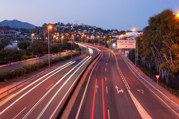 Night view of the resort town of Cala de Mijas, Spain, highway lit by lanterns with extended traces of car headlights, the inscription on the road sign "Cala de Mijas - change of direction"