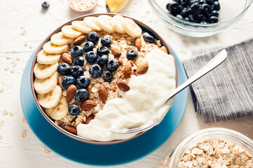 Breakfast, oatmeal with blueberry, banana almond and yogurt on a bowl in the morning.