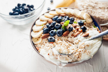 Breakfast, oatmeal with blueberry, banana almond and yogurt on a bowl in the morning.