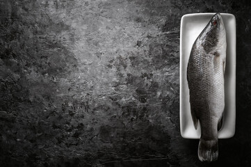 Fresh raw sea bass fish on wooden cutting board, cooking concept.