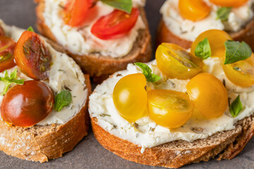 Close up of  bread slices with cream cheese and different tomato cherry  garnished with fresh basil leaves. Detail of Appetizer bruschetta or snack