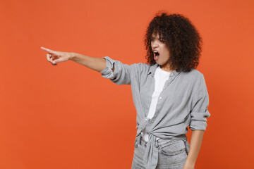 Irritated angry young african american woman girl in gray casual clothes isolated on orange background. People lifestyle concept. Mock up copy space. Pointing index finger aside, swearing screaming.