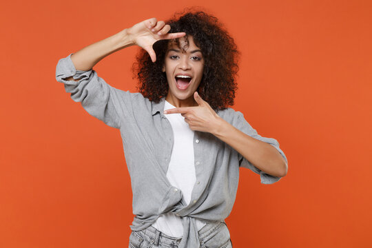 Excited young african american woman girl in gray casual clothes isolated on orange background studio portrait. People emotions lifestyle concept. Mock up copy space. Making hands photo frame gesture.