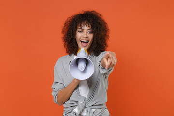 Funny young african american woman girl in gray casual clothes isolated on orange wall background. People lifestyle concept. Mock up copy space. Scream in megaphone, pointing index finger on camera.