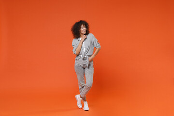 Fototapeta na wymiar Smiling young african american woman girl in gray casual clothes posing isolated on orange background in studio. People lifestyle concept. Mock up copy space. Put hand prop up on chin, looking aside.