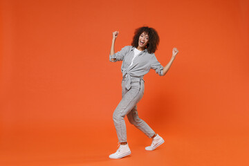 Fototapeta na wymiar Happy young african american woman girl in gray casual clothes posing isolated on orange background studio portrait. People emotions lifestyle concept. Mock up copy space. Clenching fists like winner.