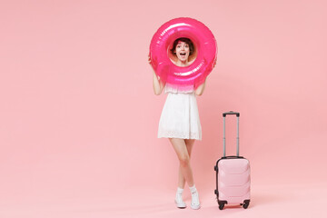 Excited tourist woman in summer dress hat with suitcase isolated on pink background. Traveling...
