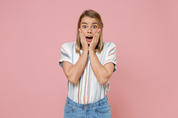 Shocked young blonde woman girl in casual striped shirt posing isolated on pastel pink background studio portrait. People sincere emotions lifestyle concept. Mock up copy space. Put hands on cheeks.