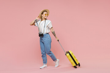Smiling girl in striped shirt glasses hat photo camera isolated on pink background. Passenger traveling abroad to travel on weekends getaway. Air flight journey concept. Hold suitcase, looking aside.