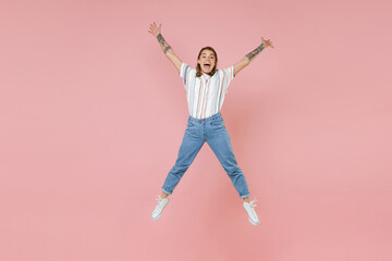 Fototapeta na wymiar Excited young blonde woman girl in casual striped shirt posing isolated on pastel pink background studio portrait. People emotions lifestyle concept. Mock up copy space. Jump spreading hands and legs.