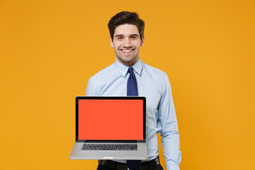 Smiling young business man in classic blue shirt tie isolated on yellow background. Achievement career wealth business concept. Mock up copy space. Hold laptop pc computer with blank empty screen.
