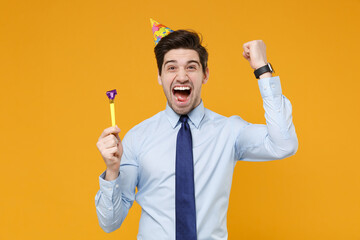 Screaming young business man in classic blue shirt tie birthday hat isolated on yellow wall...