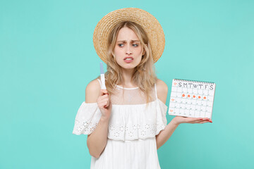 Worried young woman girl in white dress hat hold periods calendar for checking menstruation days pregnancy test isolated on blue turquoise background studio. Medical healthcare gynecological concept.