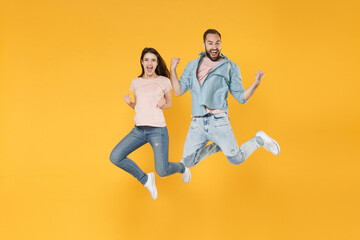 Fototapeta na wymiar Happy young couple two friends guy girl in pastel blue casual clothes posing isolated on yellow background studio portrait. People lifestyle concept. Mock up copy space. Jumping, doing winner gesture.