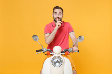 Secret young bearded guy in summer clothes driving moped isolated on yellow background. Driving...