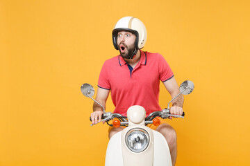 Shocked young bearded man guy in casual summer clothes helmet driving moped isolated on yellow...