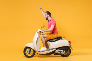 Side view excited young bearded man guy in casual summer clothes driving moped isolated on yellow background. Driving motorbike transportation concept. Mock up copy space. Rising hand clenching fist.