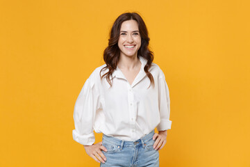 Smiling young brunette business woman in white shirt posing isolated on yellow background studio portrait. Achievement career wealth business concept. Mock up copy space. Standing with arms akimbo.