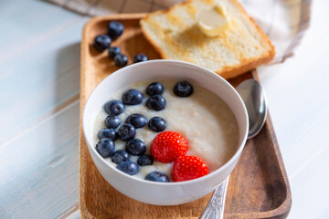 Oatmeal with fresh strawberry and blueberry and toast with butter for breakfast on wooden tray..