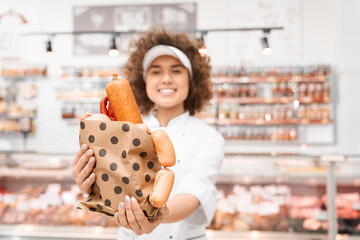 Female butcher holding bag with sausages.