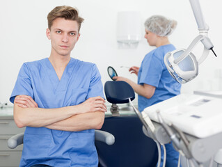 Portrait of professional male dentist with arms crossed with dental assistant background