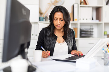 Busy female entrepreneur in office with papers and laptop